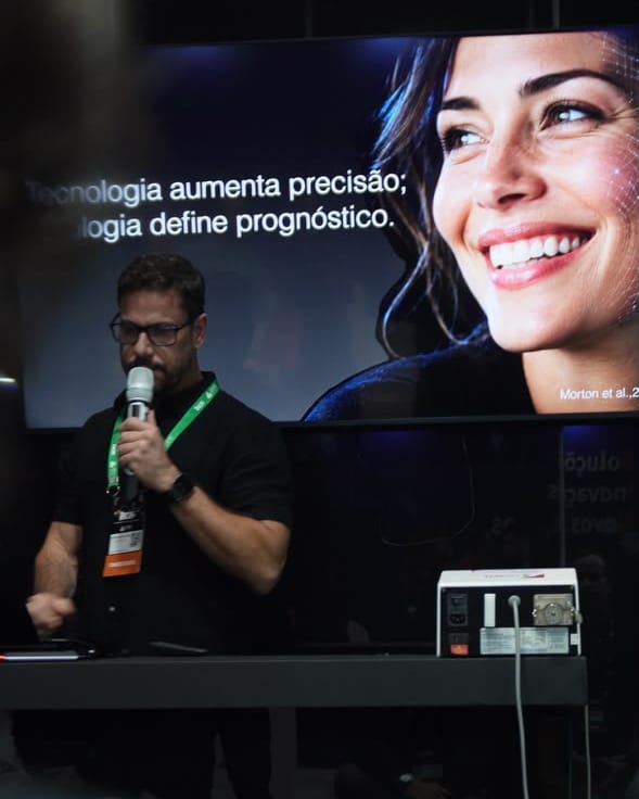 Dr. Fernando Brasil no palco, diante de um slide sobre tecnologia e precisão