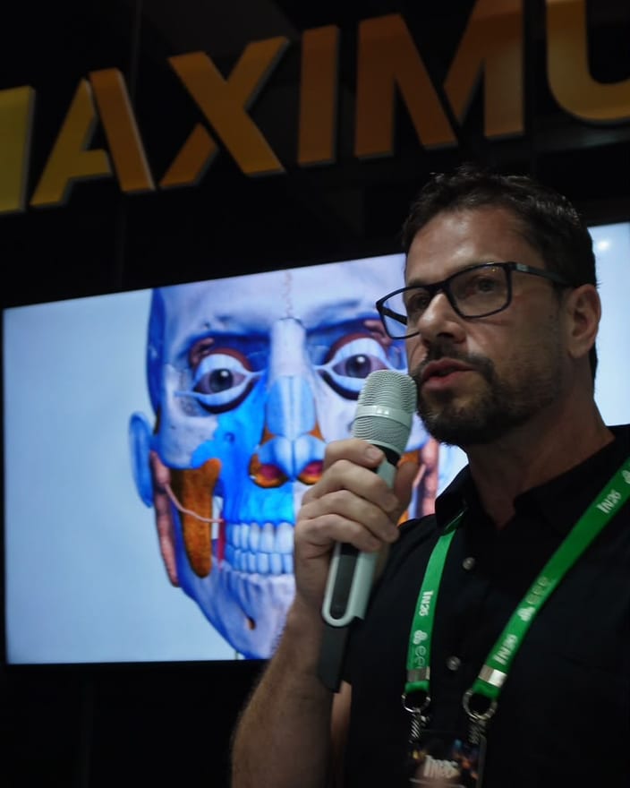 Dr. Fernando Brasil ao microfone, com um modelo 3D de anatomia da face ao fundo